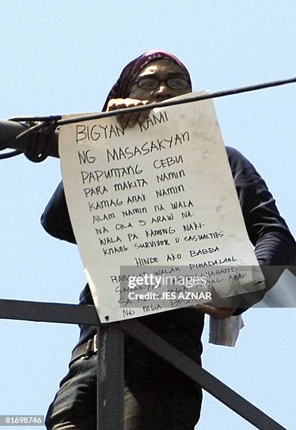 Levi Padua, a distraught relative of missing passengers of the sunken ferry MV Princess of the Stars, shows a placard as he climbs a security tower...