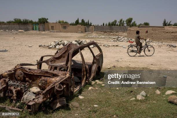 Boy rides his bike past a destroyed car on July 15, 2017 in Shadal Bazaar, Afghanistan. People are slowly returning to the recently liberated area,...