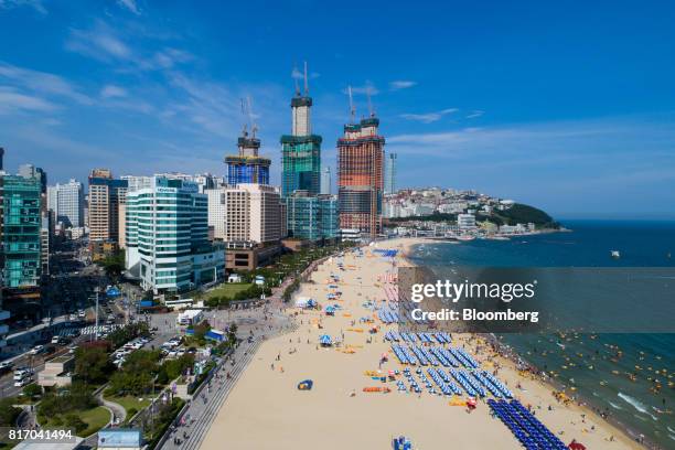 Buildings stand under construction beyond bathers on the beach and in the sea in this aerial photograph taken above Haeundae beach in Busan, South...