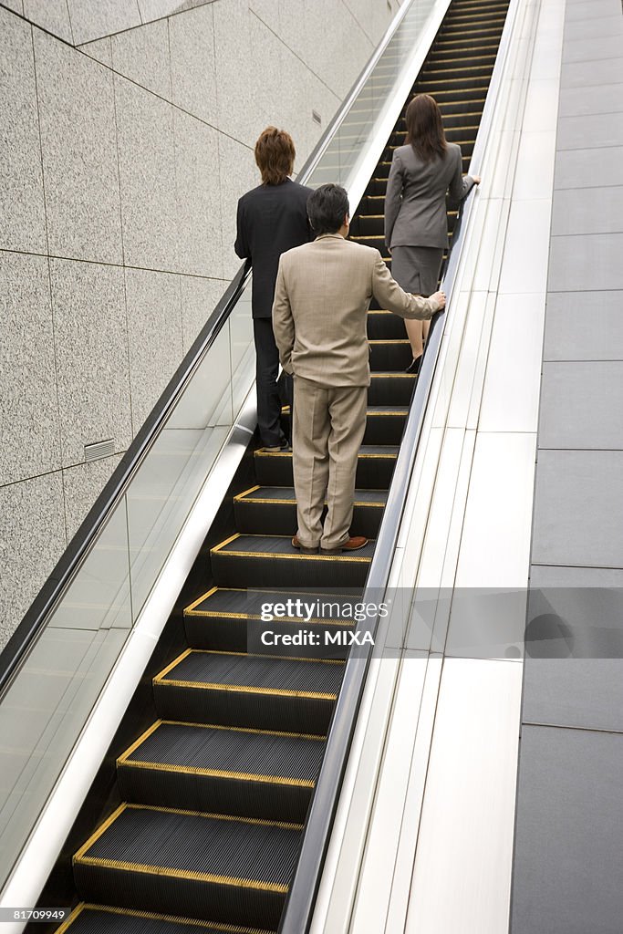 Three business people ascending escalator