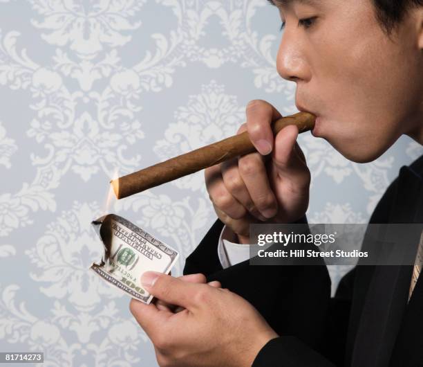 asian man lighting cigar with money - asian man smoking stock pictures, royalty-free photos & images