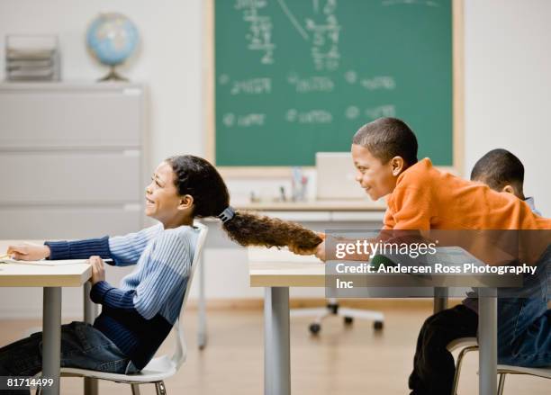 mixed race boy pulling girl's hair in school - veralbern stock-fotos und bilder