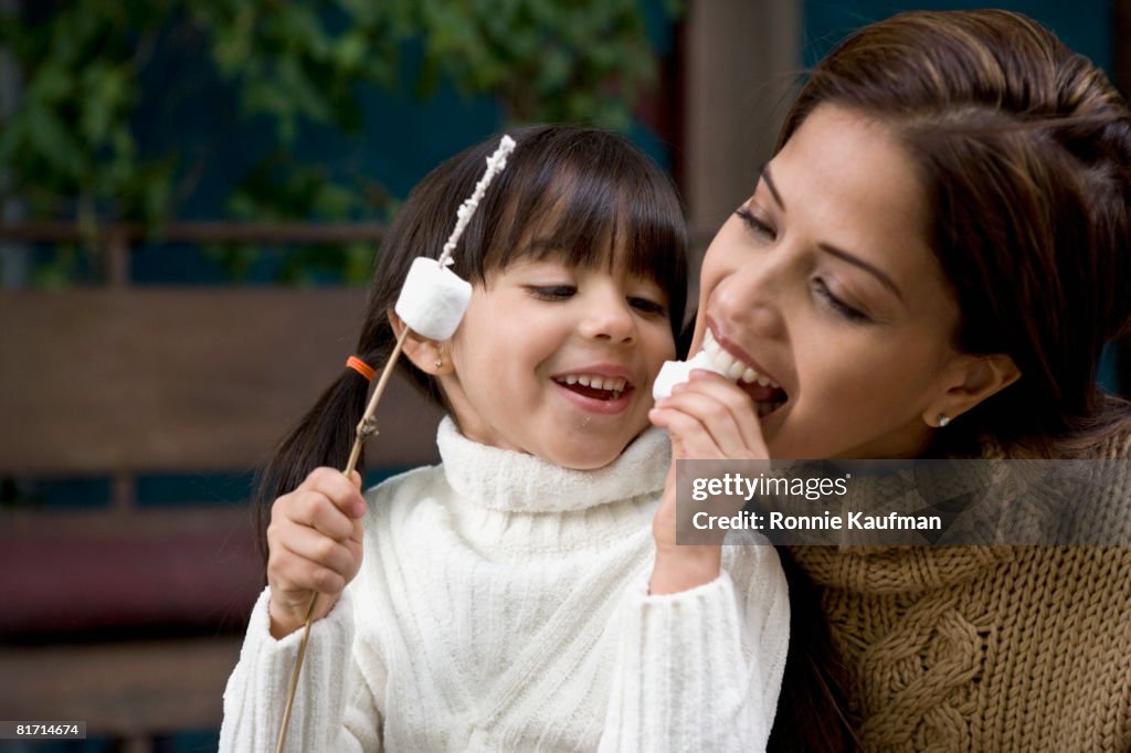 Hispanic mother and daughter eating roasted marshmallows