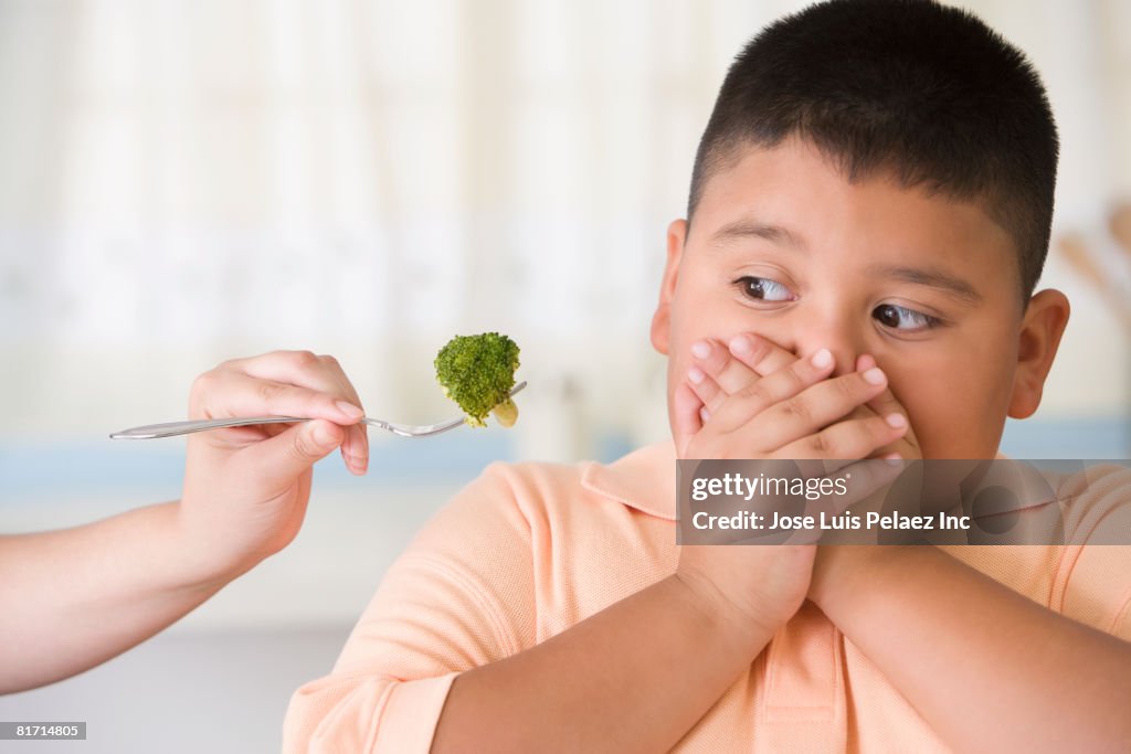 Hispanic boy covering mouth next to broccoli