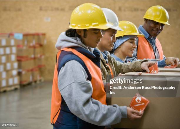 multi-ethnic warehouse workers applying warning stickers to packages - brennbar stock-fotos und bilder