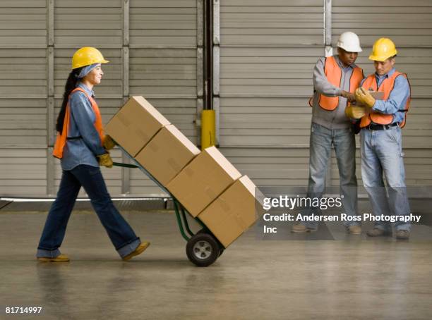 hispanic warehouse worker pushing boxes on hand truck - helmet cart stock pictures, royalty-free photos & images