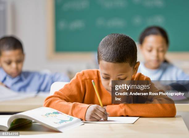 mixed race boy writing at school desk - arab student kids photos et images de collection