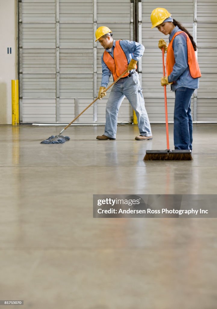 Multi-ethnic warehouse workers sweeping floor