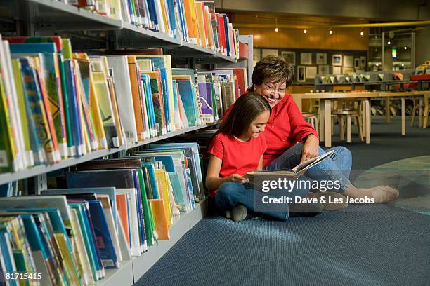 hispanic grandmother and granddaughter reading library book - jonge senioren in groep stockfoto's en -beelden