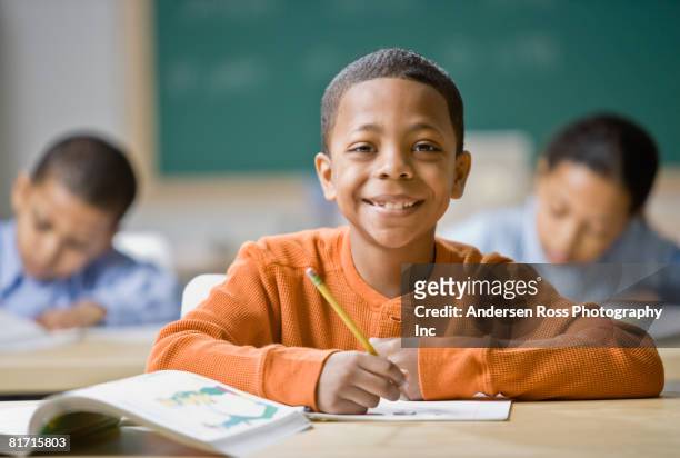 mixed race boy writing at school desk - arab student kids photos et images de collection