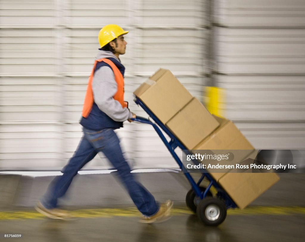 Asian warehouse worker pushing boxes on hand truck