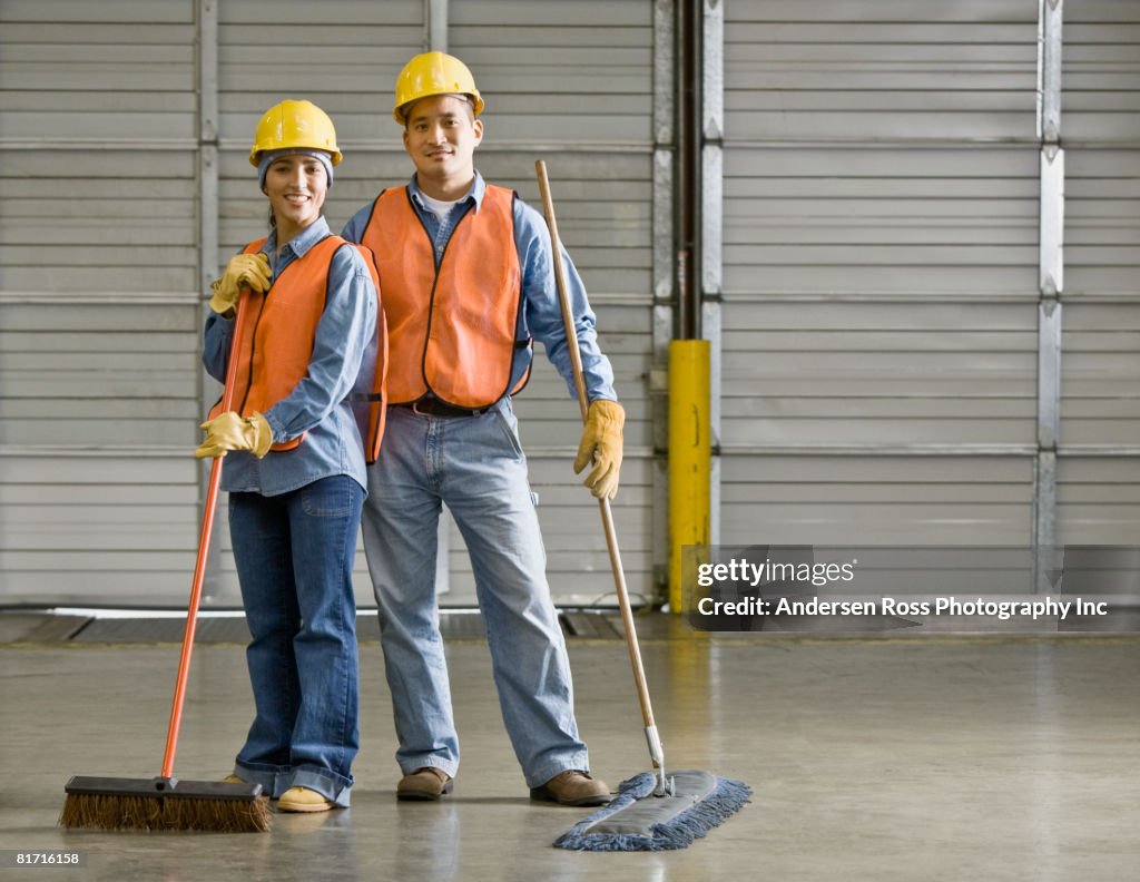Multi-ethnic warehouse workers holding brooms
