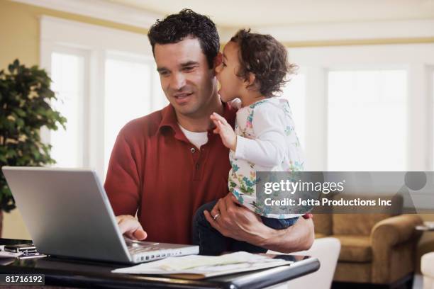 mixed race father holding baby and looking at laptop - computer work life balance stock-fotos und bilder