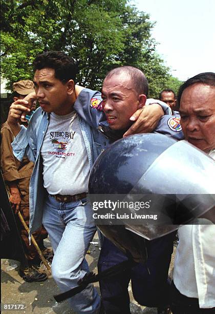 Policemen carry to safety a fellow cop hit by stones hurled by pro-Estrada demonstrators May 1, 2001 in Manila, Philippines. A May Day rally by...