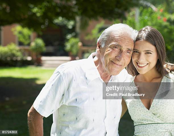 senior man standing outdoors with arm around woman smiling - old man young woman stock pictures, royalty-free photos & images
