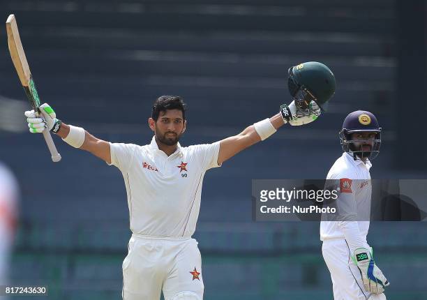 Zimbabwe cricketer Sikandar Raza raises his bat in celebration after scoring 100 runs as Sri Lanka's wicket keeper Niroshan Dickwella looks on during...