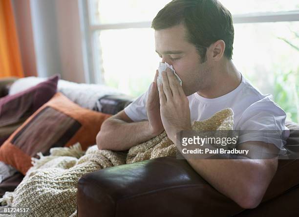 man sitting in living room blowing nose - blowing nose stock pictures, royalty-free photos & images