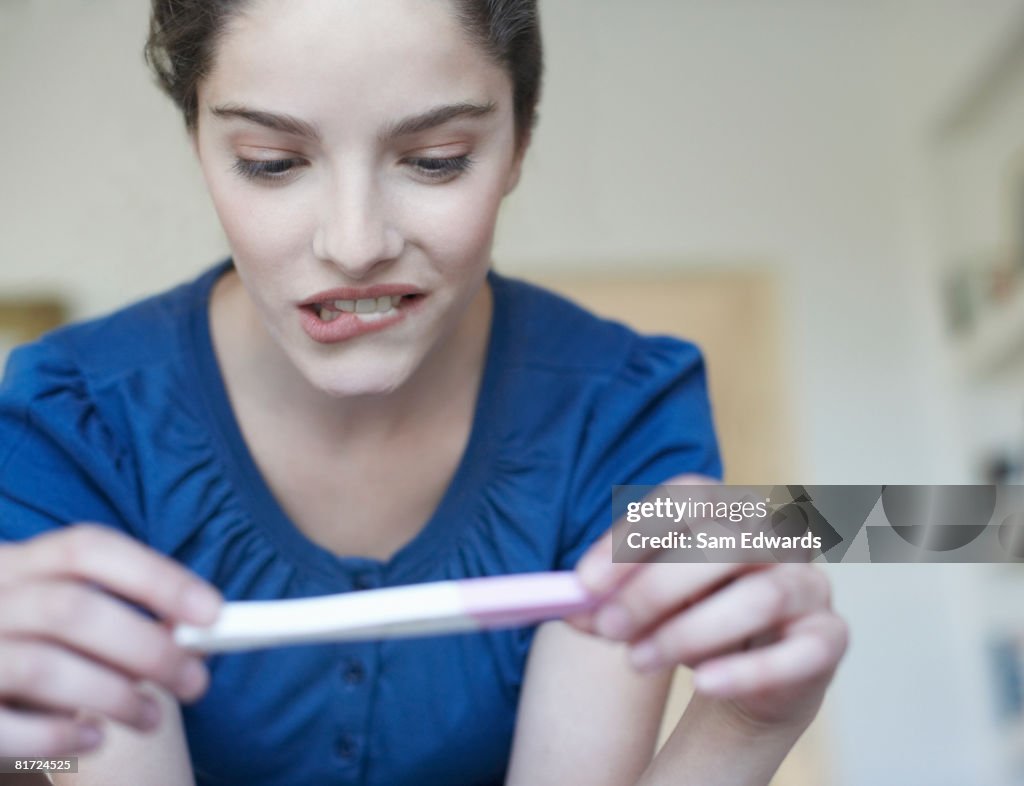 Woman holding home pregnancy test and looking worried