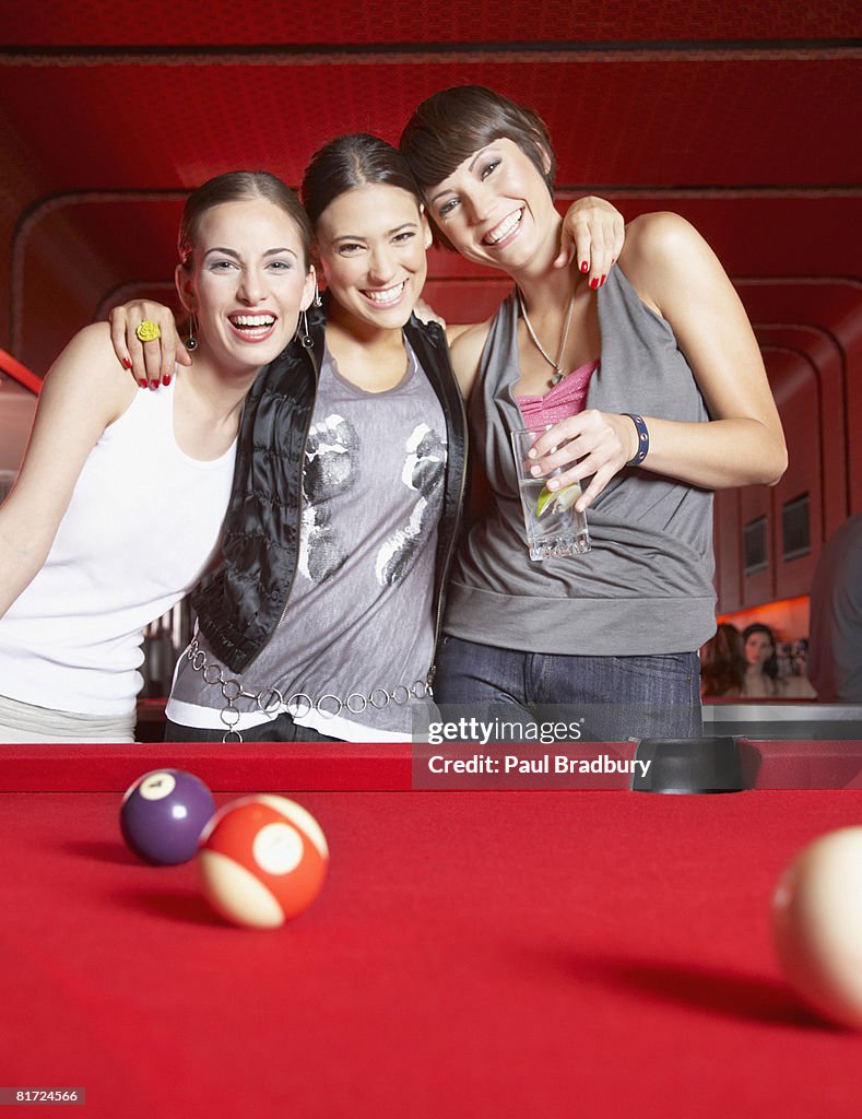 Three women standing by pool table smiling
