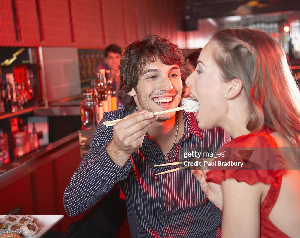 Man feeding woman sushi in nightclub and smiling