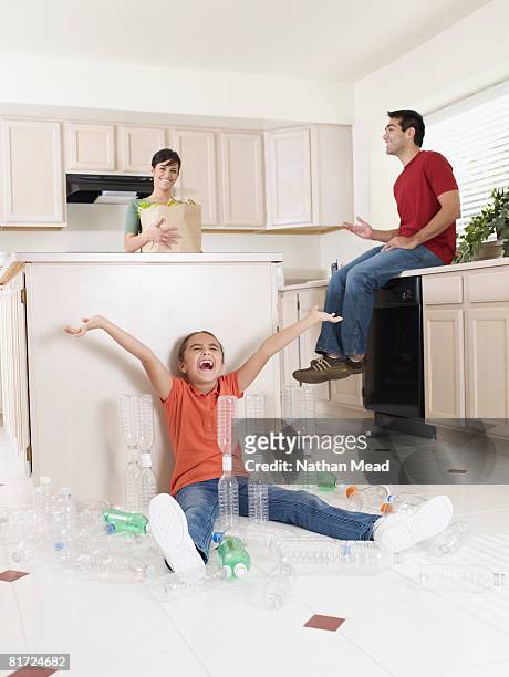 young girl sitting on kitchen floor playing with plastic bottles and couple with groceries smiling - arm made of vegetables stock pictures, royalty-free photos & images
