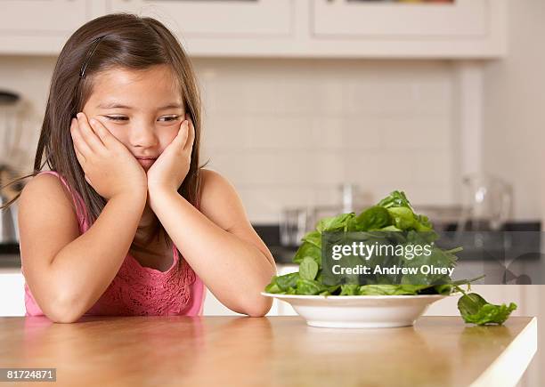 young girl in kitchen with a plate of spinach looking unhappy - eating spinach stock pictures, royalty-free photos & images