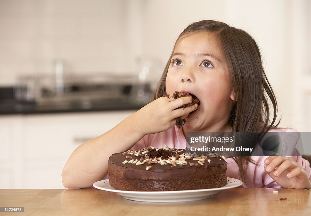 Young girl in kitchen being messy eating cake