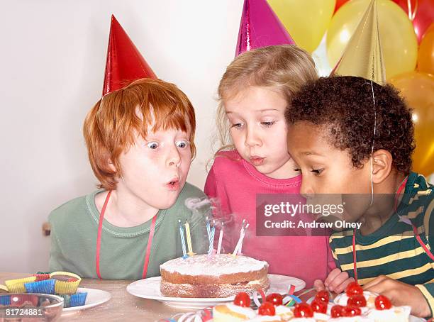 three kids at a birthday party blowing out candles on cake - solo bambini foto e immagini stock