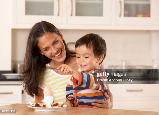 woman in kitchen with young boy eating a boiled egg and toast - kid boiled egg stock pictures, royalty-free photos & images