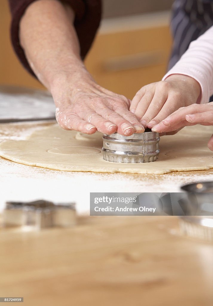 Woman and young girl in kitchen cutting out shapes in dough on counter