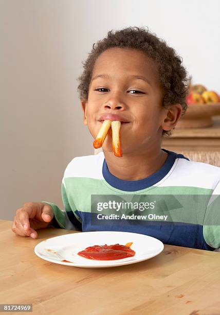 young boy in kitchen with french fries hanging out of his mouth - ketchup bildbanksfoton och bilder