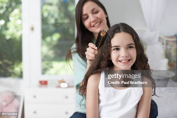 young girl in bedroom having hair brushed by woman and smiling - brushing hair stock pictures, royalty-free photos & images