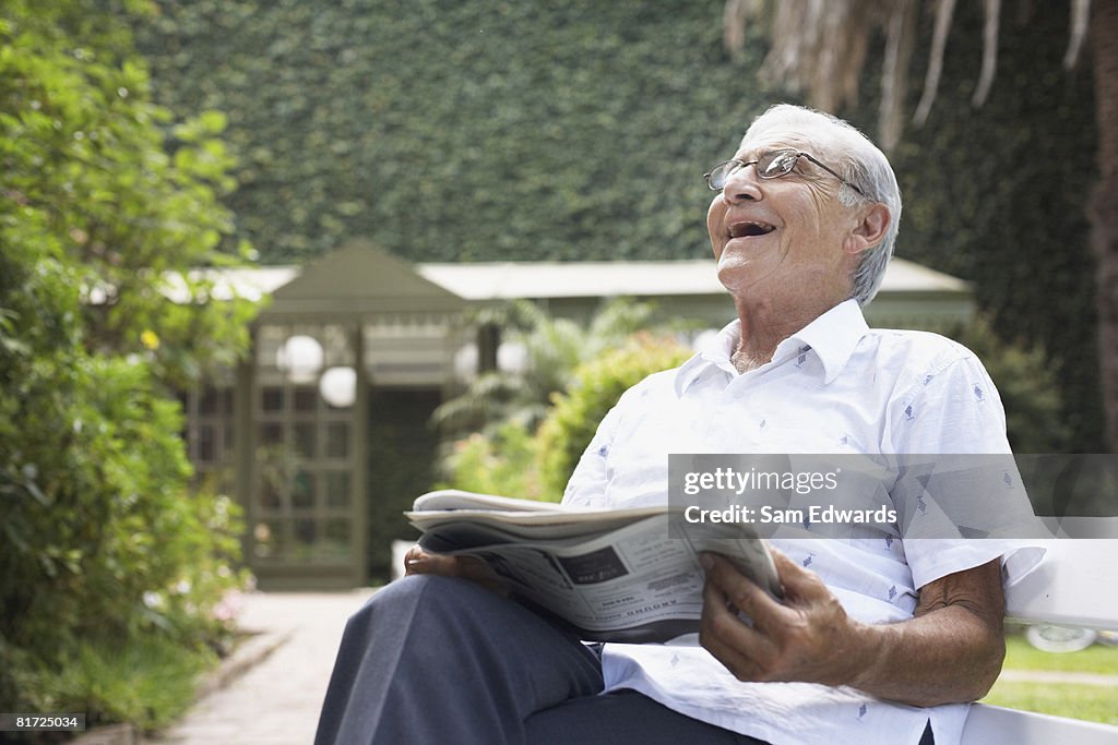 Senior homme assis à l'extérieur avec un journal rire