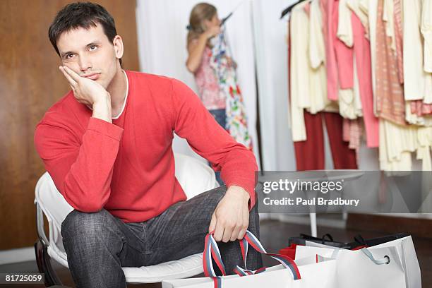 man sitting in store waiting and looking bored - boyfriend stockfoto's en -beelden