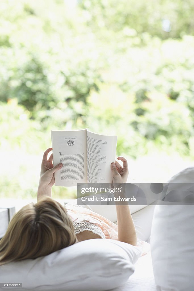Woman outdoors relaxing on patio lounger reading a book