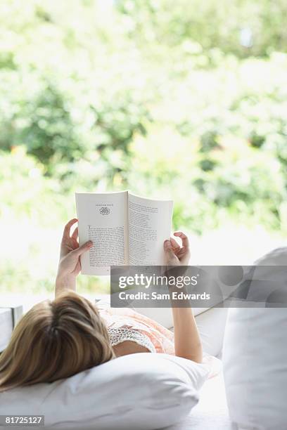 woman outdoors relaxing on patio lounger reading a book - escapism reading stock pictures, royalty-free photos & images