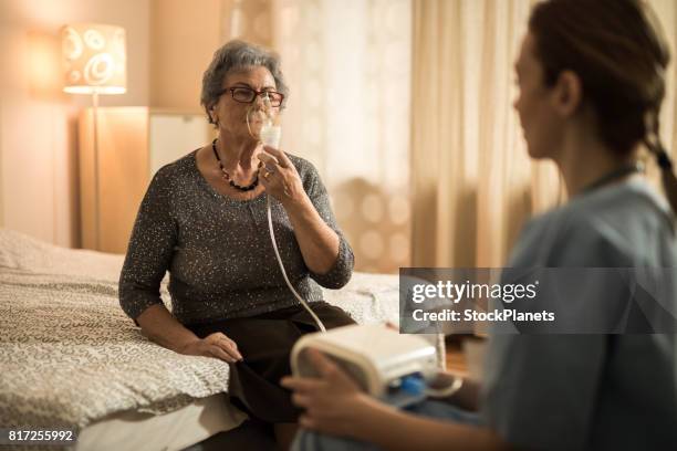 elderly woman breathing through oxygen mask during home therapy. - oxygen stock pictures, royalty-free photos & images