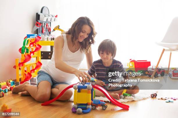 cute pregnant mother and child boy playing together indoors at home with toys - pyramid shapes around the house stock-fotos und bilder