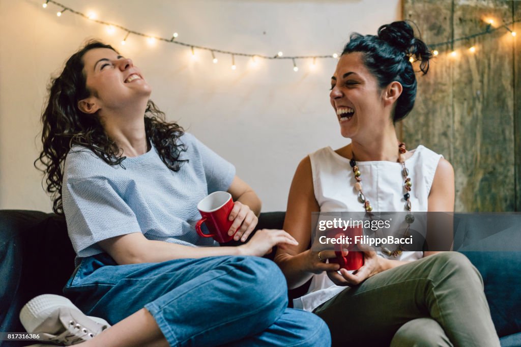 Dos amigos sentados en un sofá tomando café juntos