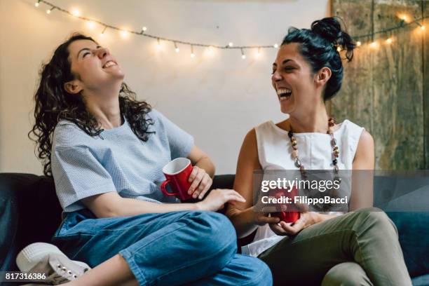 two friends sitting on a sofa drinking coffee together - sharing coffee stock pictures, royalty-free photos & images