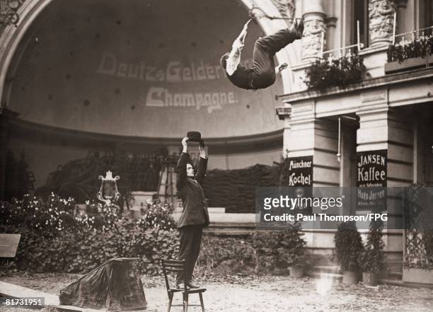 Acrobat Gerhardi Mohr somersaults over a man standing on a chair in Berlin, whilst training for his feat of leaping over a house, circa 1910.