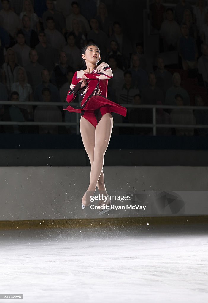 Young woman figure skater mid-air performing a triple axel.