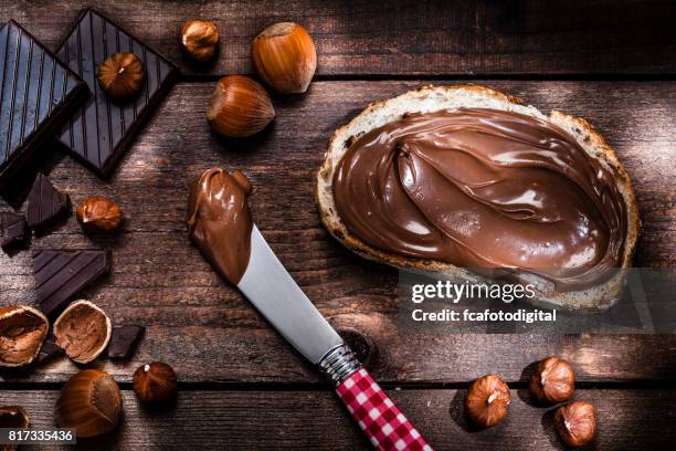 chocolat et noisette étalé sur une tranche de pain tourné sur une table en bois rustique - tartine photos et images de collection