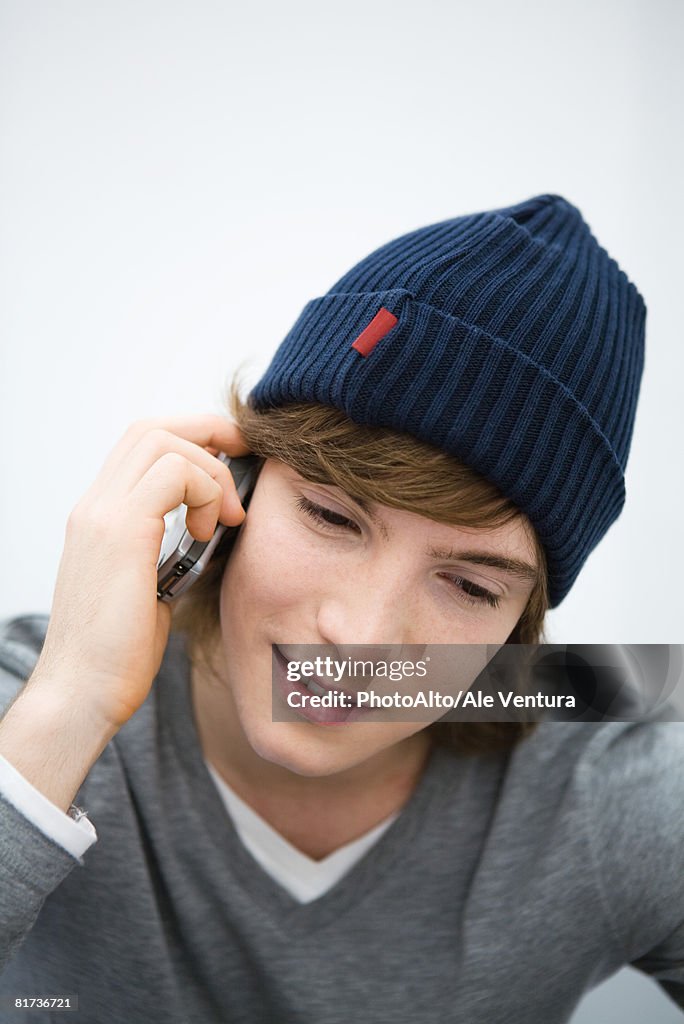 Young man in knit hat using cell phone, looking down, close-up