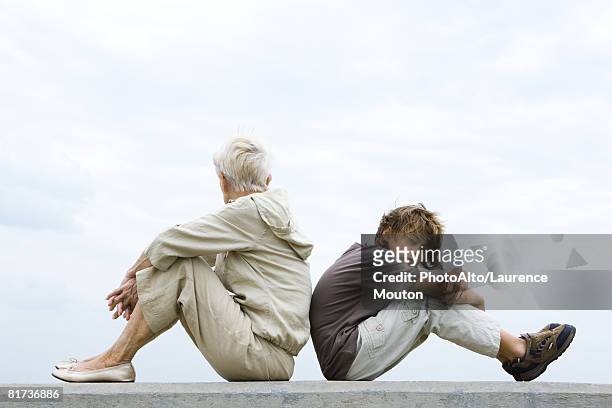 grandmother and grandson sitting back to back, woman looking away, boy looking at camera - rücken an rücken stock-fotos und bilder