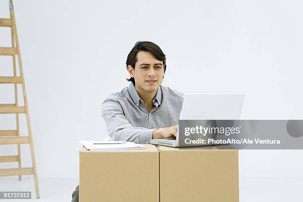 man working on laptop computer, using cardboard boxes as makeshift desk - makeshift desk stock pictures, royalty-free photos & images