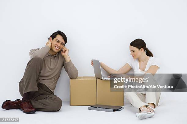 couple sitting at makeshift desk, woman using laptop computer, man using cell phone and smiling at camera - makeshift desk stock pictures, royalty-free photos & images