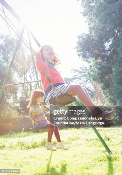 twin girls swinging in sunny backyard - solo bambine femmine foto e immagini stock