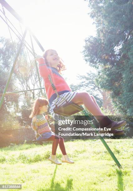 twin girls swinging in sunny backyard - alleen meisjes stockfoto's en -beelden