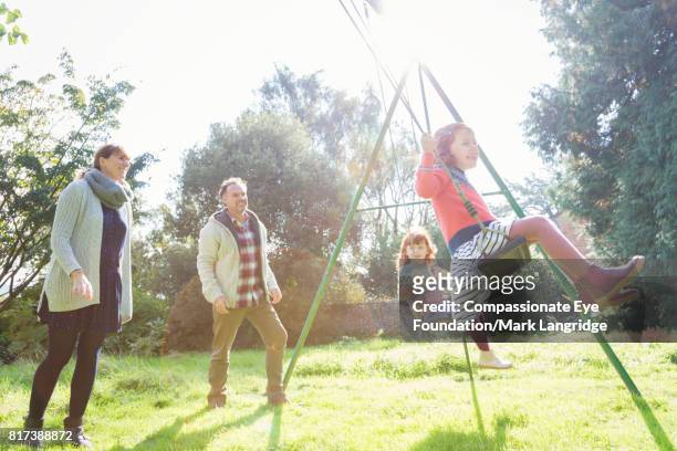 parents pushing twin girls on swings in sunny backyard - family garden play area photos et images de collection